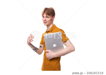 a young guy with short red hair dressed in a summer T-shirt holds a laptop in his hands on a white 108281510
