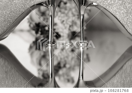 Elegant white bridal heels and wedding ring on a reflective surface, with a luxuriously blurred room backdrop. 108281768