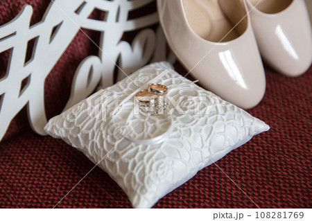 Elegant white bridal heels and wedding ring on a reflective surface, with a luxuriously blurred room backdrop. Elegant white bridal heels and wedding ring on a reflective surface, with a luxuriously blurred room backdrop. 108281769