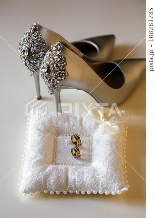 Elegant white bridal heels and wedding ring on a reflective surface, with a luxuriously blurred room backdrop. 108281785