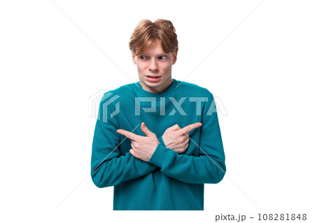 young handsome red-haired man with a blue sweater points his finger at the advertising space young handsome red-haired man with a blue sweater points his finger at the advertising space 108281848