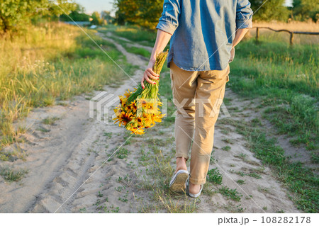 Back view, woman walking on road with bouquet of flowers, sunset light 108282178