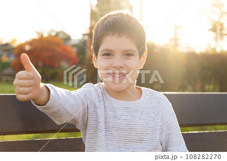 Little handsome young brunette boy showing thumbs up while looking at camera. Little handsome young brunette boy showing thumbs up while looking at camera. 108282270