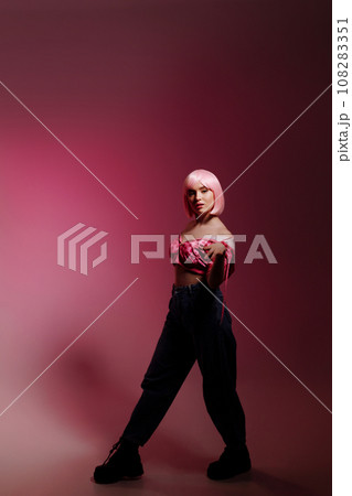 A female model stands on a pink background at a photo shoot in the studio. 108283351