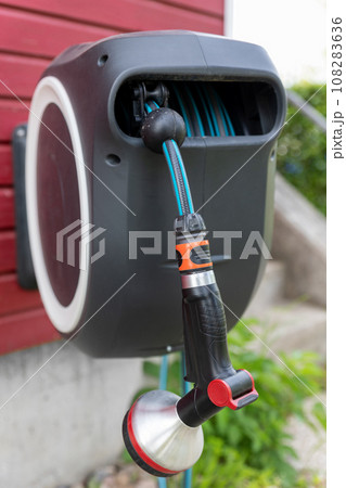 Wall Mounted Retractable Hose Reel. Modern garden lawn watering tip hose with sprinkler hanged at home wall. Lawn and plant tree smart irrigation water system equipment tool 108283636