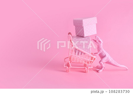 Pink Friday concept. Funny pink dinosaur toy with shopping cart full of present boxes on pink background 108283730