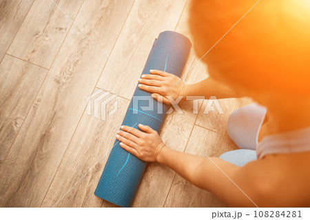 Woman hands rolled up yoga mat on gym floor in yoga fitness training room. Home workout woman close up hands rolling foam yoga gym mat. Woman barefoot home workout sportive healthy lifestyle concept 108284281