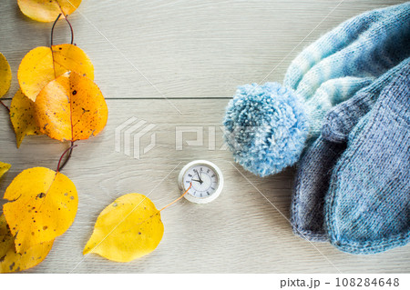 Autumn foliage, winter mittens and a clock on a wooden table. Autumn foliage, winter mittens and a clock on a wooden table. 108284648