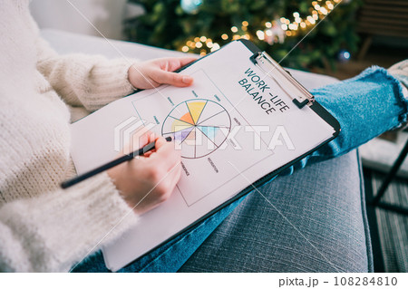 Woman drawing work-life balance wheel sitting on the sofa at home. Self-reflection and life planning for next new year. Personal Year review. Coaching tools. Finding Balance in Life. Selective focus. Woman drawing work-life balance wheel sitting on the sofa at home. Self-reflection and life planning for next new year. Personal Year review. Coaching tools. Finding Balance in Life. Selective focus. 108284810