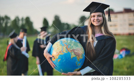 Graduate student girl poses with a globe in a meadow. 108285333