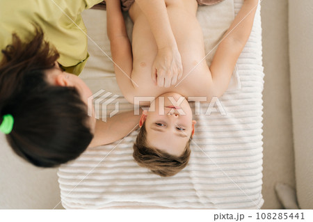 Top view portrait of professional female osteopath adjusting chest of five year old boy lying on massage table. Cute child receiving physiotherapy massage during session with chiropractor. Top view portrait of professional female osteopath adjusting chest of five year old boy lying on massage table. Cute child receiving physiotherapy massage during session with chiropractor. 108285441