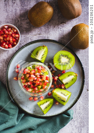 Tropical fruit kiwi, fresh yogurt and pomegranate seeds in a glass top and vertical view 108286201