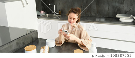 Attractive young cheerful girl baking at the kitchen, making dough, holding recipe book, having ideas Attractive young cheerful girl baking at the kitchen, making dough, holding recipe book, having ideas 108287353