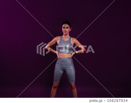 Young confident sportswoman in silver fitness attire with hands on hips Young confident sportswoman in silver fitness attire with hands on hips 108287834