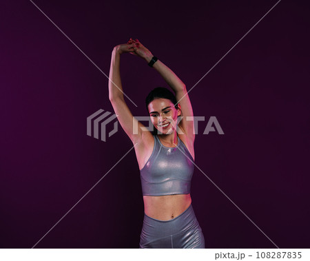 Positive woman in silver sportswear flexing her hands on a magenta background Positive woman in silver sportswear flexing her hands on a magenta background 108287835