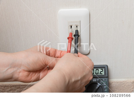 【テスターでコンセントの電圧を計る主婦】 108289566