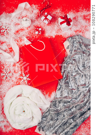 Festive Christmas attributes and decorations on a red background. Gift boxes and sequin dress on the snow. Red paper package. 108290771