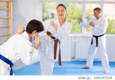 Woman and man in pairs exercising karate movements during group training in gym 108293354