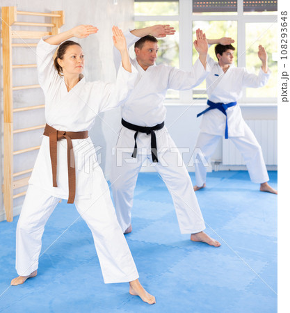 Woman and man in kimono standing in fight stance during group karate training in gym 108293648