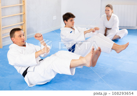 Woman and men in kimono train abdominal muscles and do punches at same time during karate or judo training 108293654