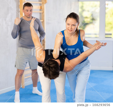 Woman training power move during self-defense training under guidance of trainer 108293656