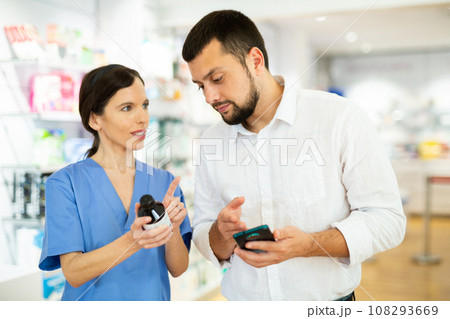 Male shopper shows name of drug on smartphone screen. Female pharmacist helps to find medicine in pharmacy 108293669