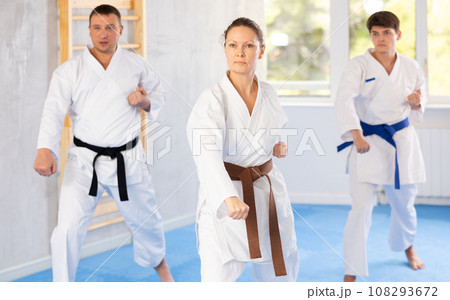 Woman and man in kimono standing in fight stance during group karate training in gym Woman and man in kimono standing in fight stance during group karate training in gym 108293672
