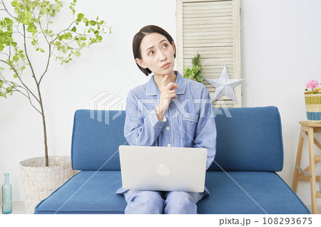 リビングでパジャマ姿でノートパソコンを使いながら考える女性 108293675