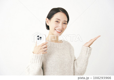 スマートフォンを持って手のひらで右側を指す女性　白背景 108293966