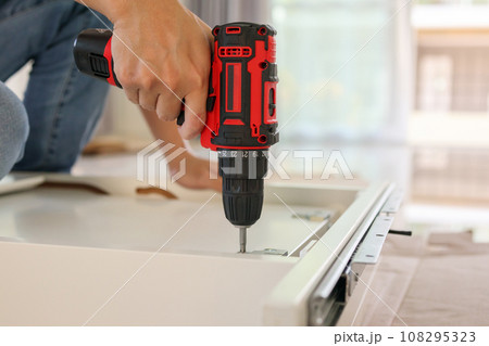 man assembling white table furniture at home using cordless screwdriver 108295323