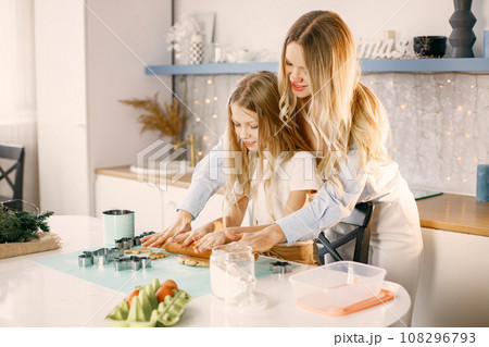 Family preparation of ginger biscuits with daughter. Mother and little girl cooking cookies. Blonde woman wearing blue shirt and girl white t-shirt. 108296793