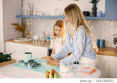 Family preparation of ginger biscuits with daughter. Mother and little girl cooking cookies. Blonde woman wearing blue shirt and girl white t-shirt. Family preparation of ginger biscuits with daughter. Mother and little girl cooking cookies. Blonde woman wearing blue shirt and girl white t-shirt. 108296801