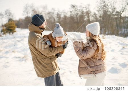 Portrait of happy family having fun on winter walk. Mother, fater and son hugging. Family wearing warm jacket and knitted hats. 108296845
