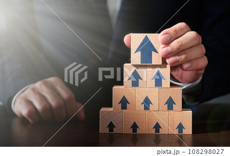 ビジネスの成長戦略と成功の達成のイメージ。テーブルに木のブロックを積み上げる男性。矢印のアイコンとレ 108298027
