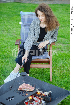Woman stirs the coals while cooking a steak on the grill Woman stirs the coals while cooking a steak on the grill 108299626