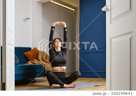 Young woman doing stretching at home sitting on yoga mat 108299641