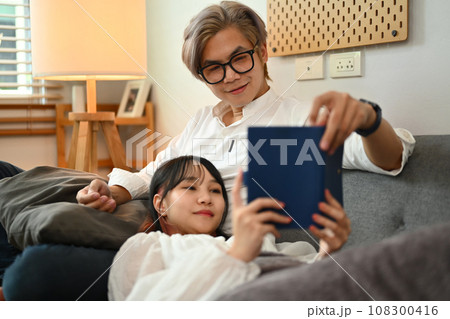 Loving young couple reading book while sitting together on sofa in living room 108300416