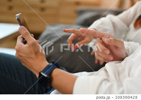 Cropped shot of young couple checking social media on smartphone relaxing together on sofa at home 108300428