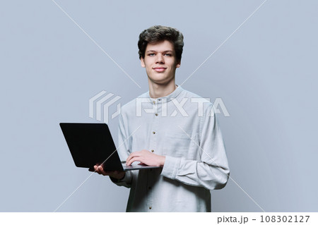 Young male college student using laptop, grey background Young male college student using laptop, grey background 108302127
