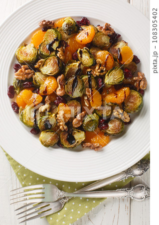 Delicious warm Brussels sprouts salad with tangerines, walnuts and dried cranberries dressed with balsamic glaze close-up in a plate on the table. Vertical top view Delicious warm Brussels sprouts salad with tangerines, walnuts and dried cranberries dressed with balsamic glaze close-up in a plate on the table. Vertical top view 108305402
