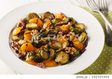 Healthy vegan Brussels sprouts salad with mandarin oranges, walnuts and dried cranberries dressed with balsamic glaze close-up in a plate. Horizontal 108305404