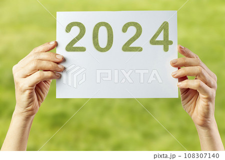 2024, Woman holding cardboard with number 2024 on green background. Happy New Year 108307140