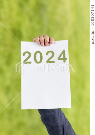 2024, Man holding cardboard with number 2024 on green background. Happy New Year 2024, Man holding cardboard with number 2024 on green background. Happy New Year 108307141