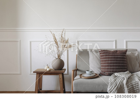 Dry grass bouquet in ball shaped vase. Midcentury sofa with cup of coffee, checkered linen cushions, blanket. Little white pumpkins, old side table. Autumn interior. Thanksgiving, Halloween. Dry grass bouquet in ball shaped vase. Midcentury sofa with cup of coffee, checkered linen cushions, blanket. Little white pumpkins, old side table. Autumn interior. Thanksgiving, Halloween. 108308019