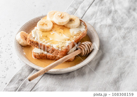 Toasts with butter, banana slices and honey on light linen background. Homemade breakfast sandwich close up. Simple food concept 108308159