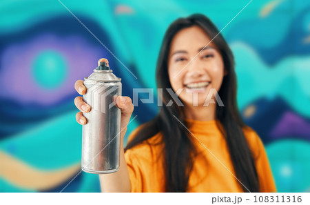 Smiling female street artist pointing spray paint can to camera 108311316