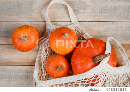 Ripe pumpkins in mesh bag on wooden background. Eco-friendly farm products. Autumn harvest and Thanksgiving concept. 108312818