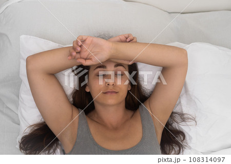 A restless soul, a young woman with long hair, lies in bed, suffering upset from battling insomnia. A restless soul, a young woman with long hair, lies in bed, suffering upset from battling insomnia. 108314097