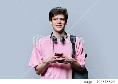 Young male with headphones holding smartphone, on grey background Young male with headphones holding smartphone, on grey background 108315527