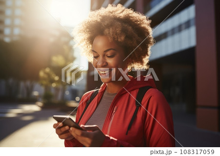 Athletic young African American woman in sports outfit with smartphone while training outdoor. Slender black lady resting after jogging or walking in city street. Active lifestyle in urban environment Athletic young African American woman in sports outfit with smartphone while training outdoor. Slender black lady resting after jogging or walking in city street. Active lifestyle in urban environment 108317059